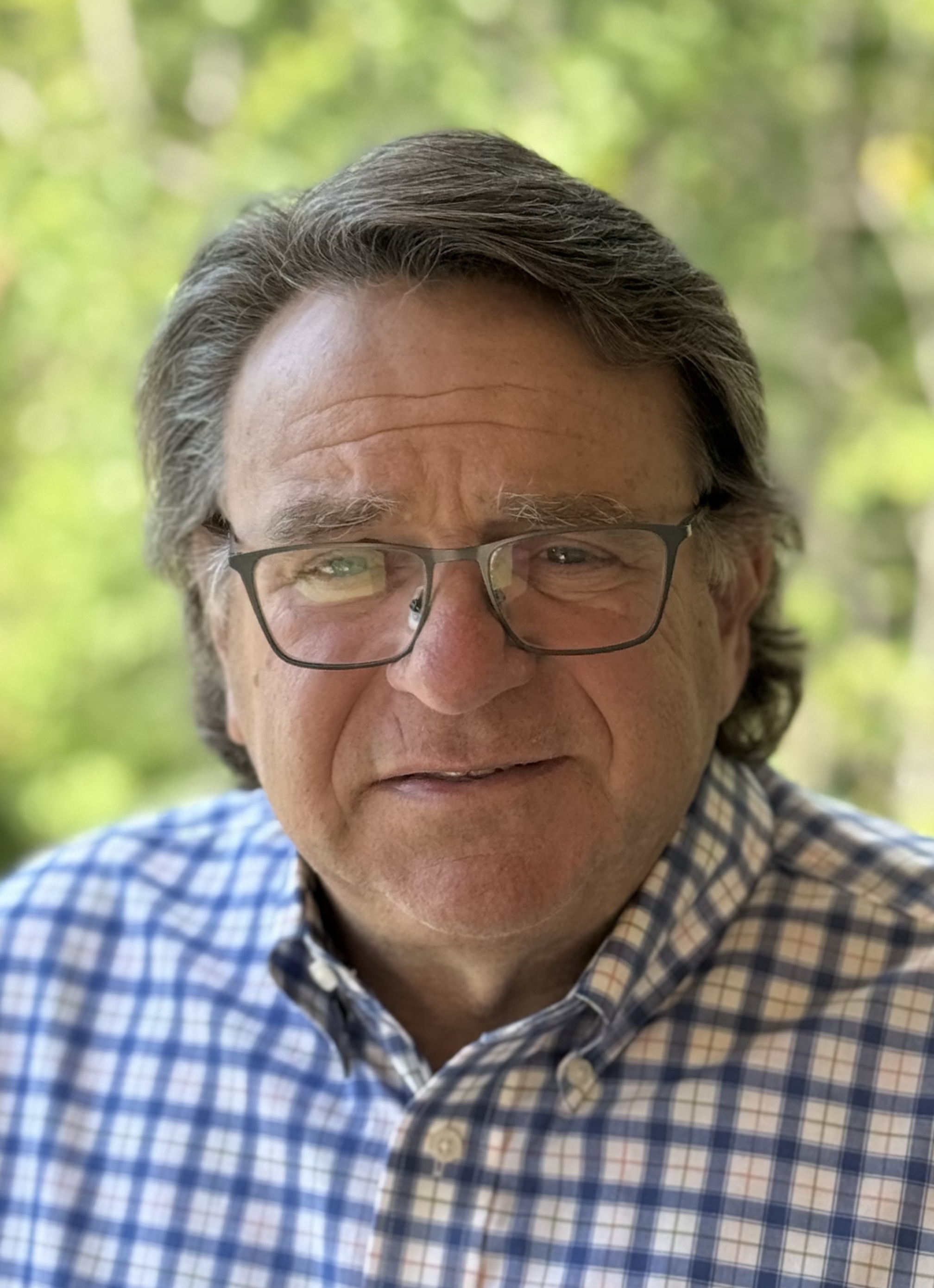 Executive coach John R. Rodgers, Jr., smiling outdoors in a checked shirt